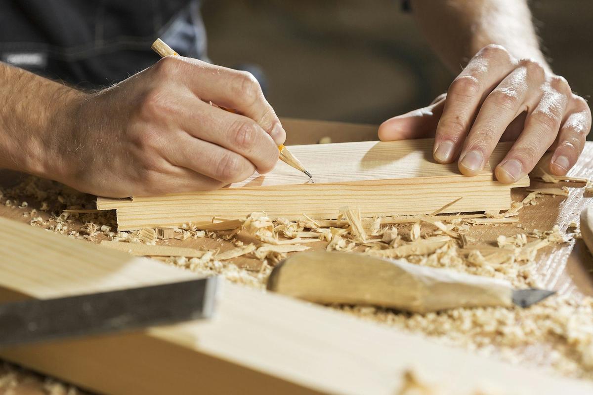 Handen die met een potlood een maat aftekenen op een houten plank