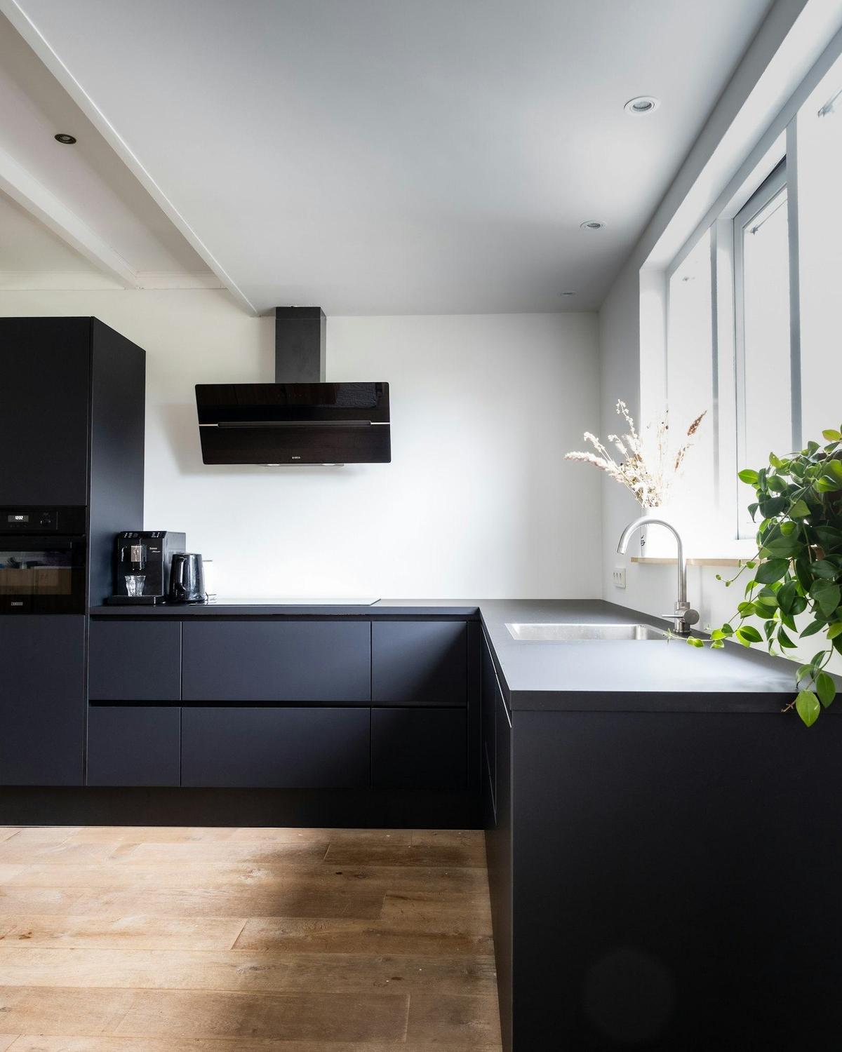 Afgewerkte keuken met matzwarte kasten, een dampkap en een eikenhouten vloer
