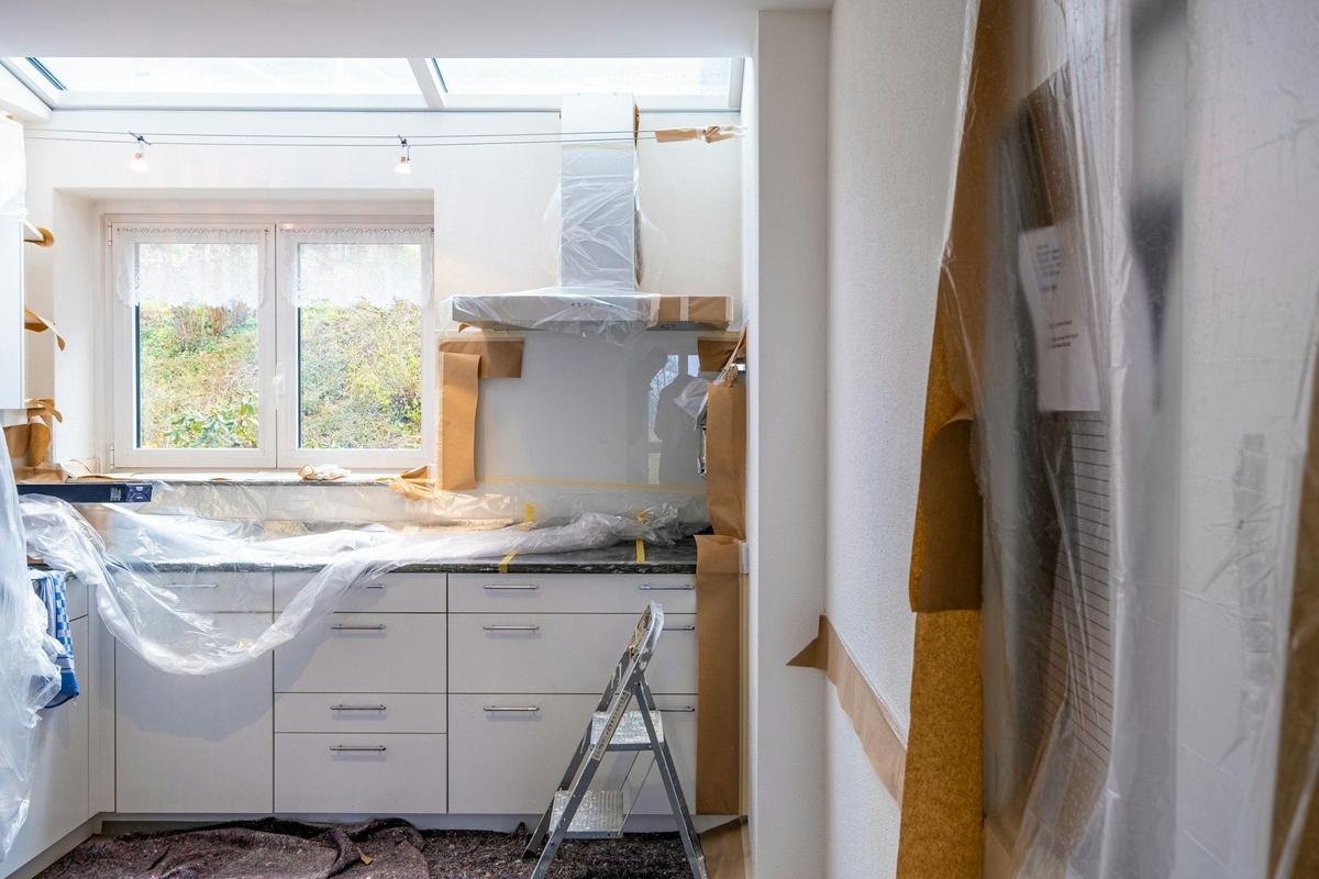 Keuken tijdens de werken: kasten onder plastic, een trapladder en een raam met tuinzicht